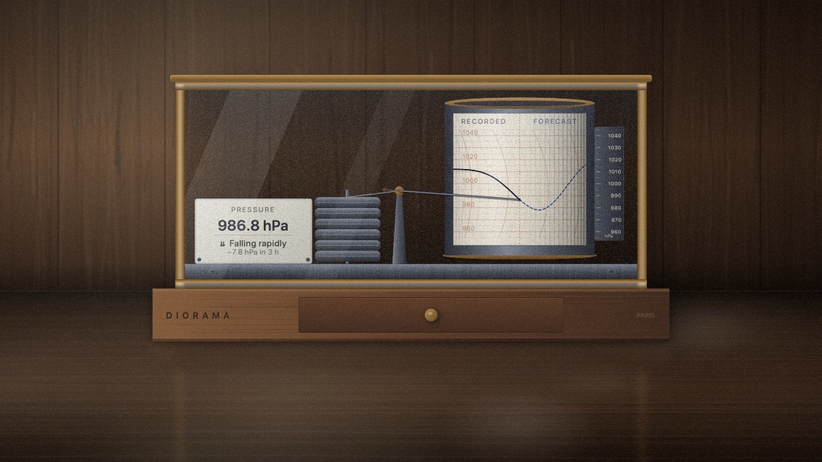 A brass-and-glass recording barometer standing on a polished walnut table, its paper drum carrying a falling pressure trace with the pen resting on it.